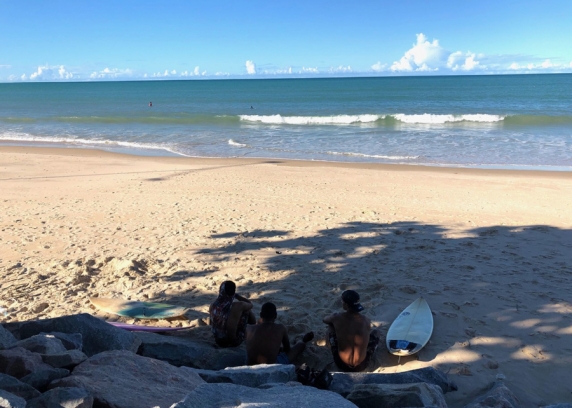 Três surfistas descansam na sombra na praia de Ponta Negra.